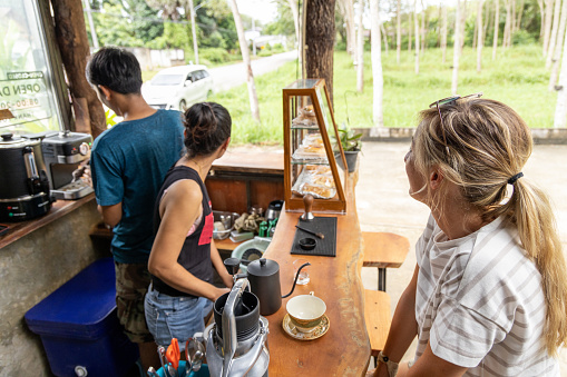 30's female having an espresso at local cafe in Thailand, small business concept. Diversity, tourist sharing with Thai owner.