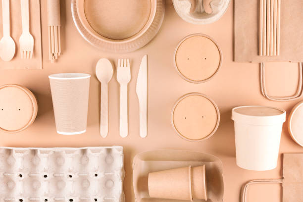 istock Food industry paper packaging - paper utensils, cups, plates, drinking straws, egg boxes, bamboo cutlery set and food containers over light brown background. Flat lay style. Food delivery service 1447062296