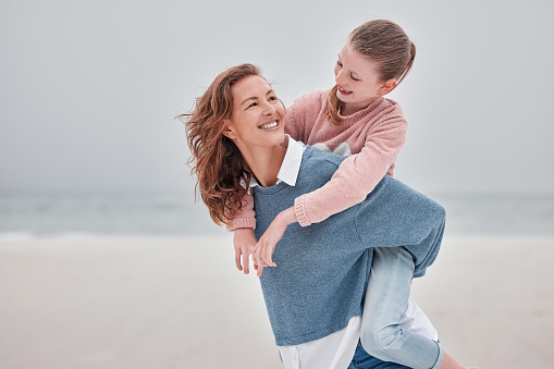 Mother, child and hug for love on beach with smile for quality bonding time together in nature. Mama and kid smiling in joyful happiness for piggyback embracing relationship on a sandy ocean coast