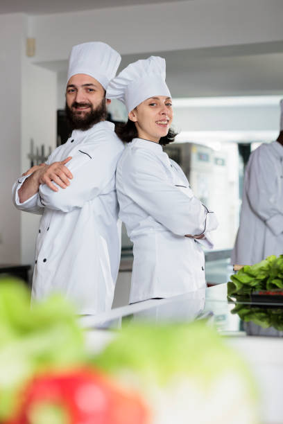 istock Skilled cooks wearing cooking uniforms while posing back to back in restaurant kitchen space. 1447065354