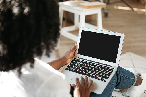 Beautiful african woman working with laptop at home in living room close up