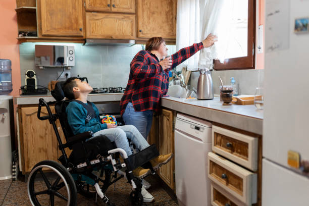 istock Hispanic mother looking through the window in the kitchen with her disabled son in a wheelchair. Family, unconditional love and inclusion concept. 1447071933