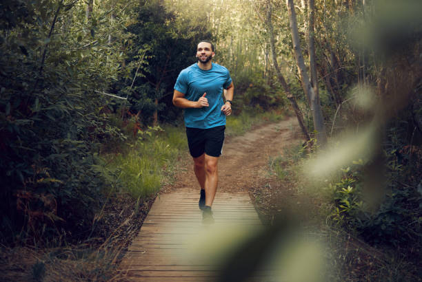 Man, running and fitness on forest path, nature woods bridge or countryside environment for health, wellness or heart health. Smile, happy or sports runner in exercise, training and workout in Canada Man, running and fitness on forest path, nature woods bridge or countryside environment for health, wellness or heart health. Smile, happy or sports runner in exercise, training and workout in Canada mens track stock pictures, royalty-free photos & images