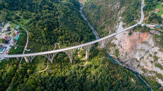 An aerial shot of the Djurdjevica Tara Bridge in Montenegro with forest-covered hills on the background