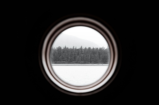 A porthole POV of a snowy landscape in the Inside Passage, Alaska