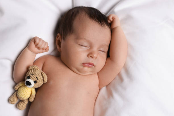 istock Cute little baby with toy bear sleeping on soft bed, top view 1447075361