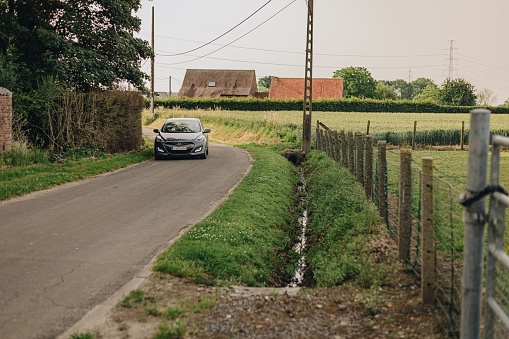 z, Belgium – June 22, 2022: A car passing by an open field in one of the countrysides of Belgium