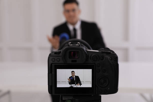 istock Business man giving interview at official event, focus on video camera screen 1447076637