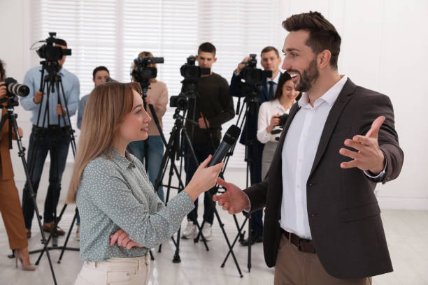 istock Professional young journalist interviewing businessman and group of video camera operators on background 1447076792