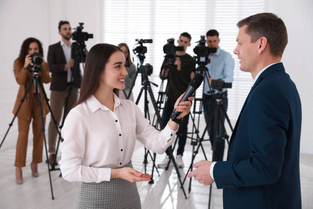 istock Professional young journalist interviewing businessman and group of video camera operators on background 1447076936