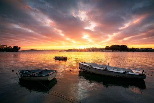 A Corun, Spain – October 21, 2022: The small boats anchored at the city harbor captured at a glowing sunrise