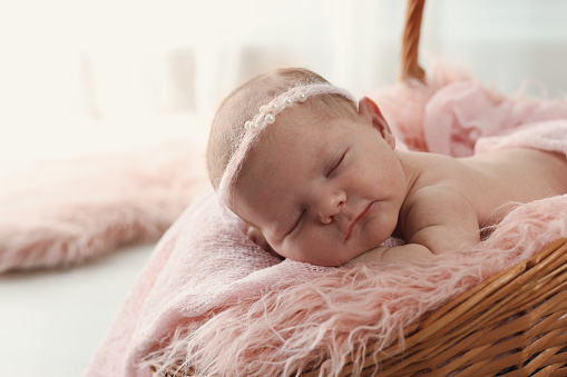 Adorable little baby sleeping in wicker basket at home