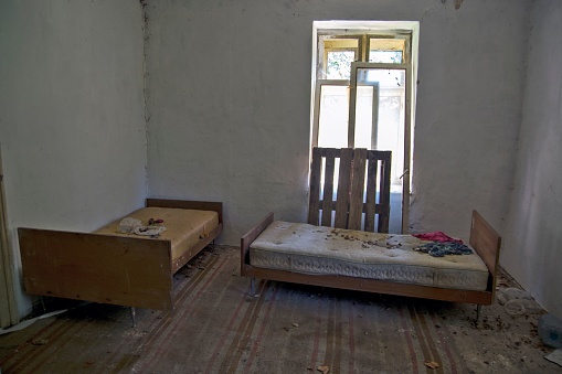 An old and abandoned bedroom of a house in the hills with dirty beds and rotting walls