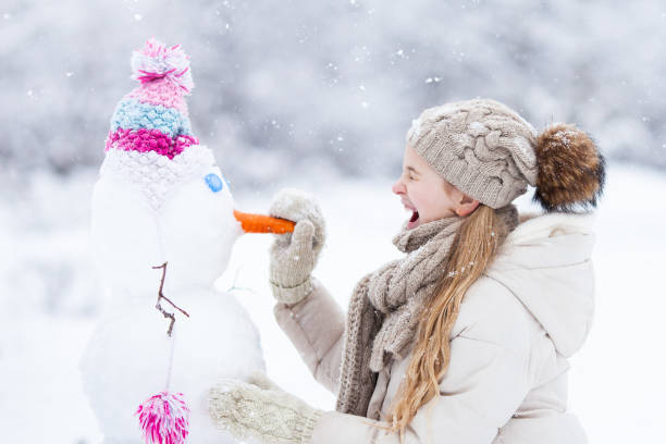 Laughing caucasian girl wearing warm knitted clothes building a snowman on a snowy day. stock photo