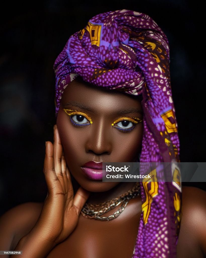 Beautiful African female with a purple headwrap on her head isolated on a dark background A beautiful African female with a purple headwrap on her head isolated on a dark background Adult Stock Photo