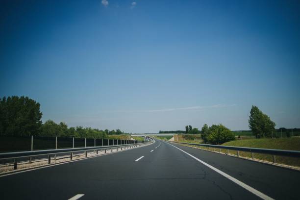 istock Asphalted road with white markings, railings, and trees beside it under a blue sky 1447084010