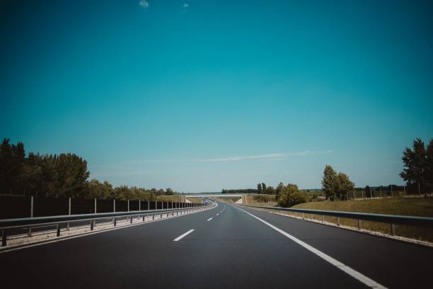 istock Empty highway road with white markings, railings and green trees beside it under a blue sky 1447084043