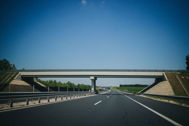 istock Empty asphalted road with white markings, railings and a small bridge over it under a clear blue sky 1447084066