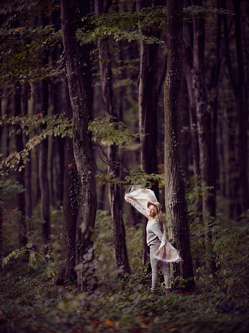 Young happy woman having fun among trees during autumn day in the forest. Copy space.