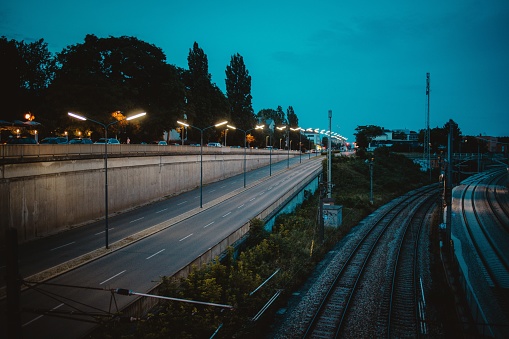 A highway with street lights near train railroads under an evening sky