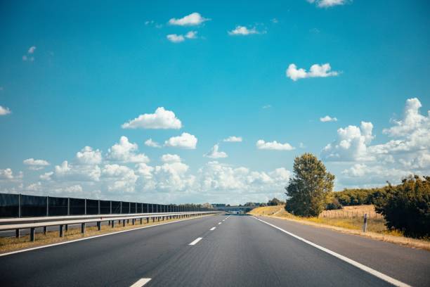 istock Empty asphalted highway road with white markings, railings, and green trees beside it 1447085415