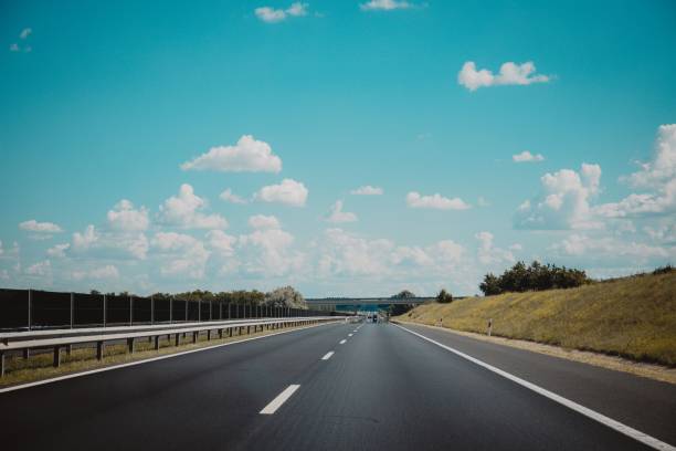 istock Empty asphalted road with white markings, railings and trees beside it under a blue sky with clouds 1447085420