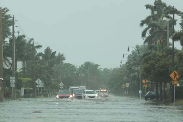 flooded road with cars passing through during hurricane nicole in palm beach, florida. november 2022 - flood hurricane road damaged imagens e fotografias de stock