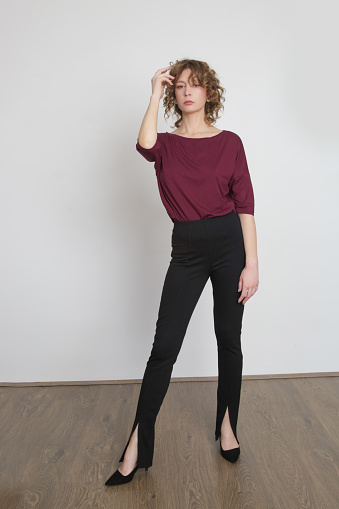 Serie of studio photos of young female model wearing simple comfortable outfit, organic cotton burgundy blouse and black skinny trousers	with slits