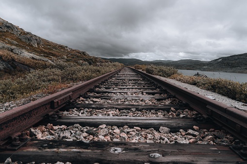 Old railroad with wooden ties and gravel ballast on a rocky hill against a cloudy sky