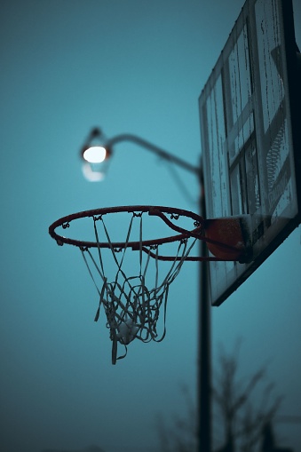 A vertical shot of a basketball hoop on the blurry background