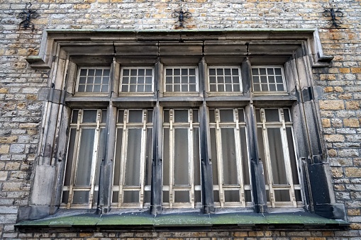 A low angle closeup of old wooden windows on a stone brick facade of a building