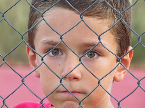 A portrait of a sad Caucasian boy that immigrated from Ukraine behind a wire fence