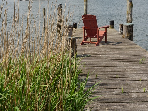 A wooden pier over the river with a red folding chair isolated on it