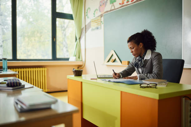 African American teacher writing her plans in the classroom.