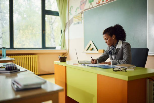 professora afro-americana escrevendo seus planos na sala de aula. - grading teacher desk writing - fotografias e filmes do acervo