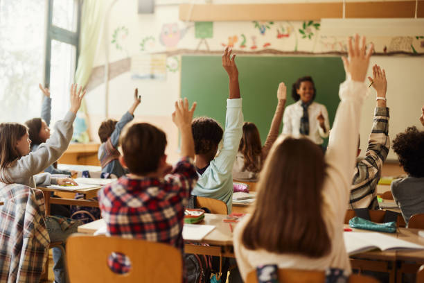 istock Rear view of students raising their hands to answer the teacher's question on a class. 1447095194