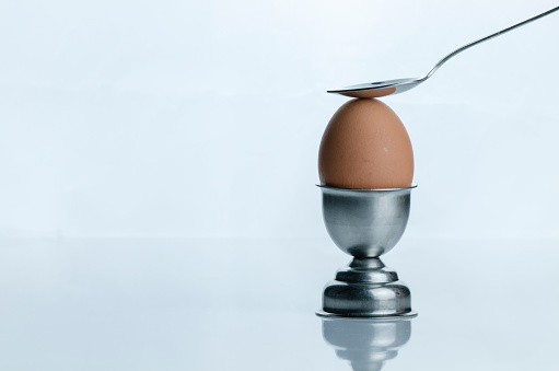 Soft boiled egg on egg cup with spoon against white background