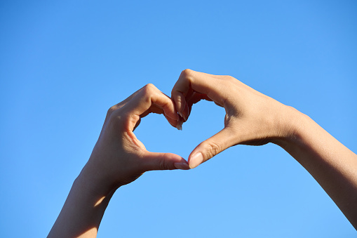 A woman making a heart with her hands under the blue sky