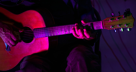Close up man hands playing guitar on stage live in concert with neon lights.