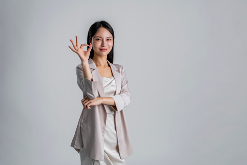 Young beautiful woman over isolated gray background smiling positive doing ok sign with hand and fingers.