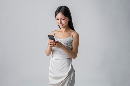 Young asian female texting on her phone against a gray background