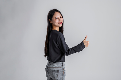 Excited asian woman isolated on gray background and gesturing thumbs up