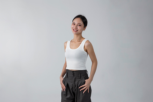 Young laughing woman standing with hands in pockets, wearing blank white shirt with copy space, isolated on gray background