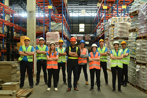 Group of warehouse worker standing in line with arms crossed together at logistic distribution warehouse. Corporate team concept.