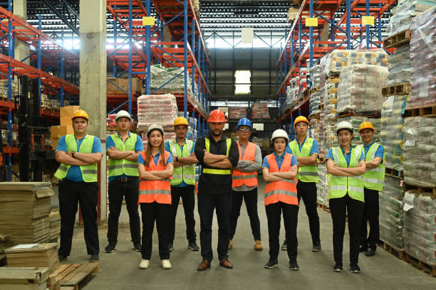 Group of warehouse worker standing in line with arms crossed together at logistic distribution warehouse. Corporate team concept. Group of warehouse worker standing in line with arms crossed together at logistic distribution warehouse. Corporate team concept. manufacturing occupation photos stock pictures, royalty-free photos & images