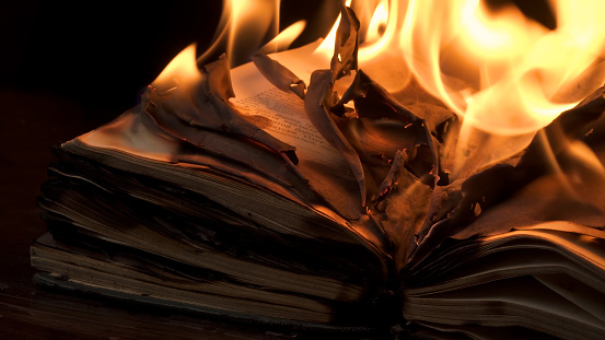 An open book is on fire. Big bright flame, burning paper on old publication in the dark. Book Burning - Censorship Concept