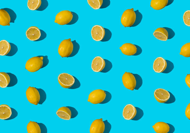 istock Summer pattern made with fresh cut and whole yellow lemon on bright light blue background. Minimal background summer concept on with harsh light and sharp shadow 1447105620