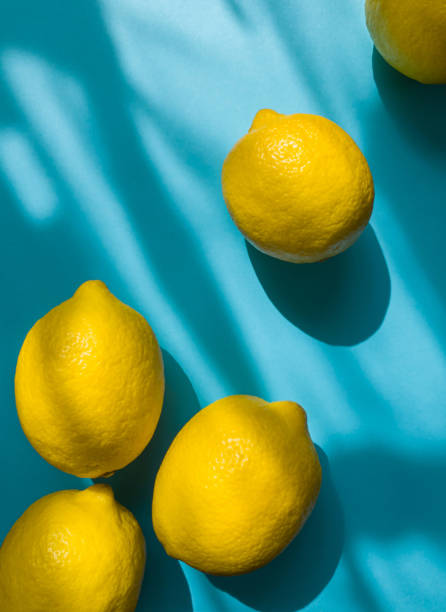istock Composition with whole ripe yellow lemons on bright blue background. Summer time flat lay with daylight and sharp shadows. Top view 1447106454