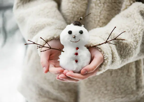 Little cute smiling snowman in the child hands. Having fun in wintertime. Selective focus. Copy space.