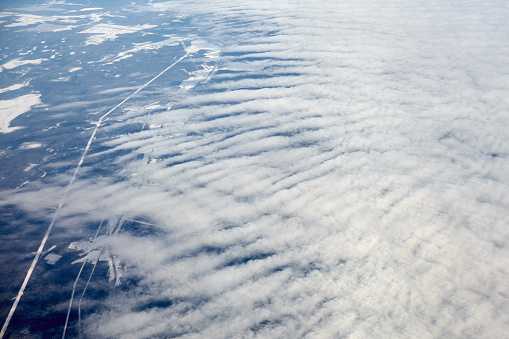 Aerial view from airplane window over clouds top to snow covered rivers, fields and roads, winter fresh frosty air. Beautiful hazed sky aerial view to Earth troposphere, snowy background texture
